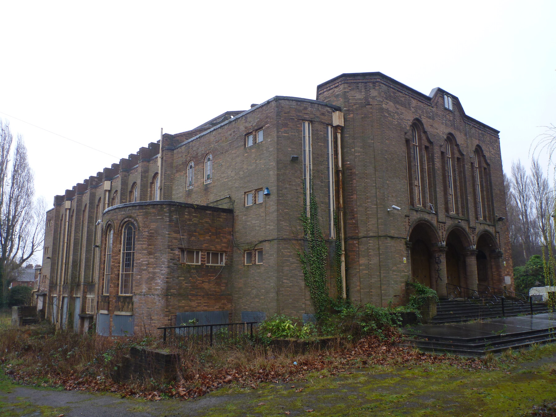 The former Greenbank Drive Synagogue in Sefton Park, showing its large 1930s brick exterior and overgrown grounds.
